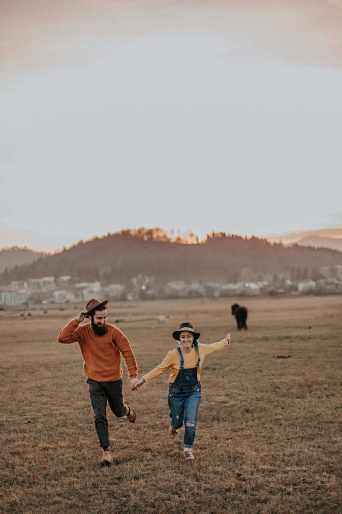 Pareja con sombreros corriendo por el campo