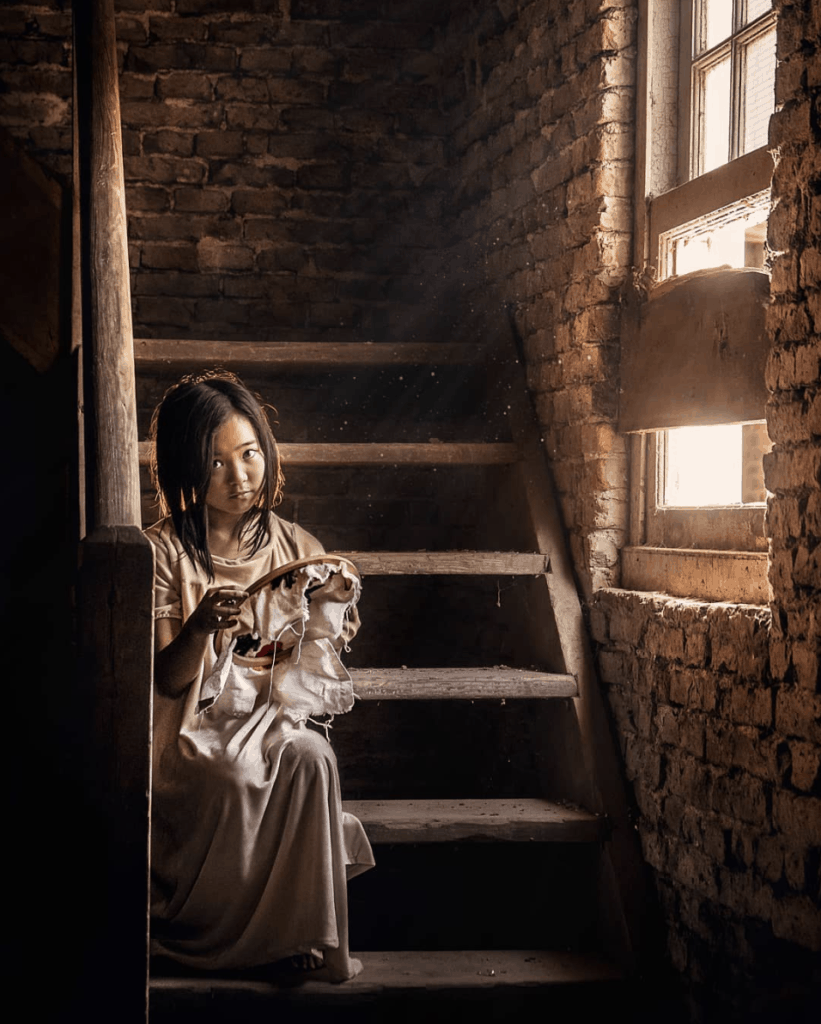 niña bordando bajo luz ventana