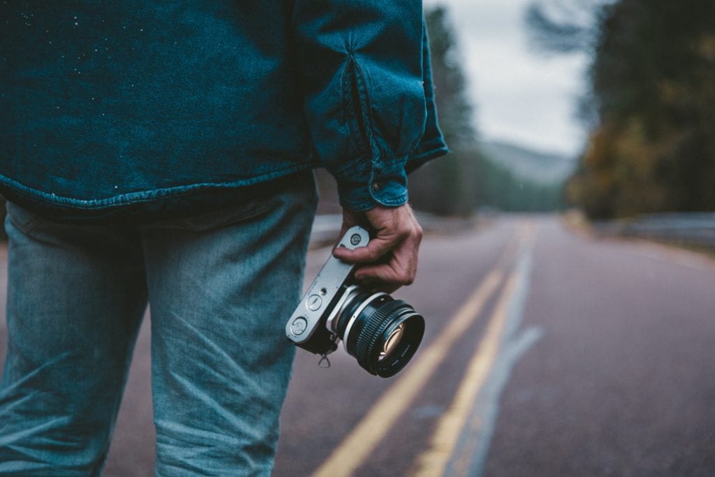 Cámara fotográfica en la mano con carretera de fondo