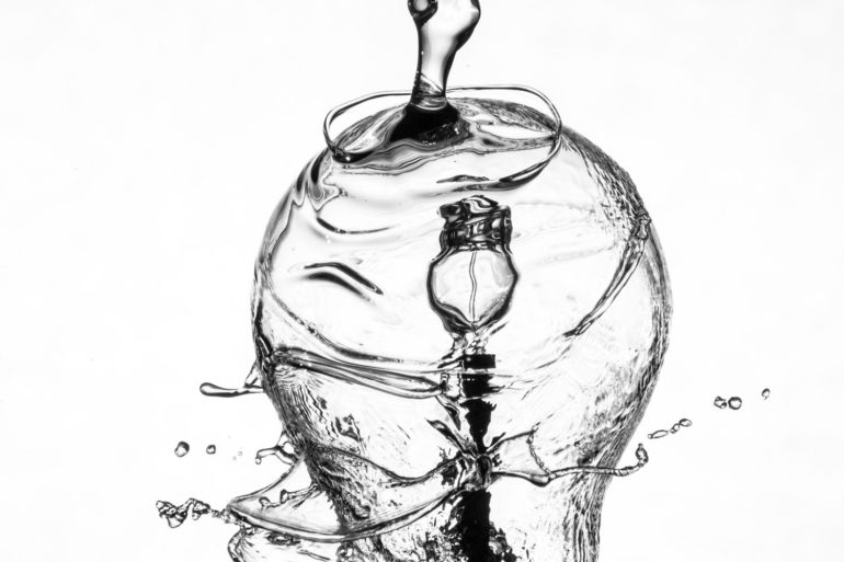 Bombilla bañada por chorro de agua sobre fondo blanco