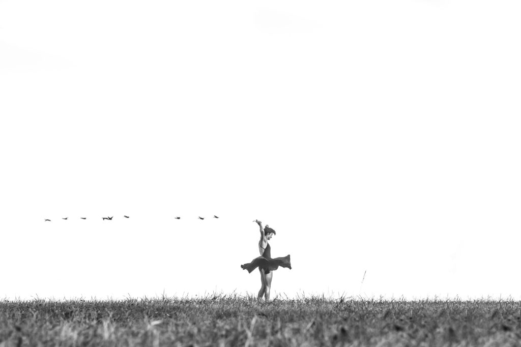 Bailarina en medio del campo con pájaros volando