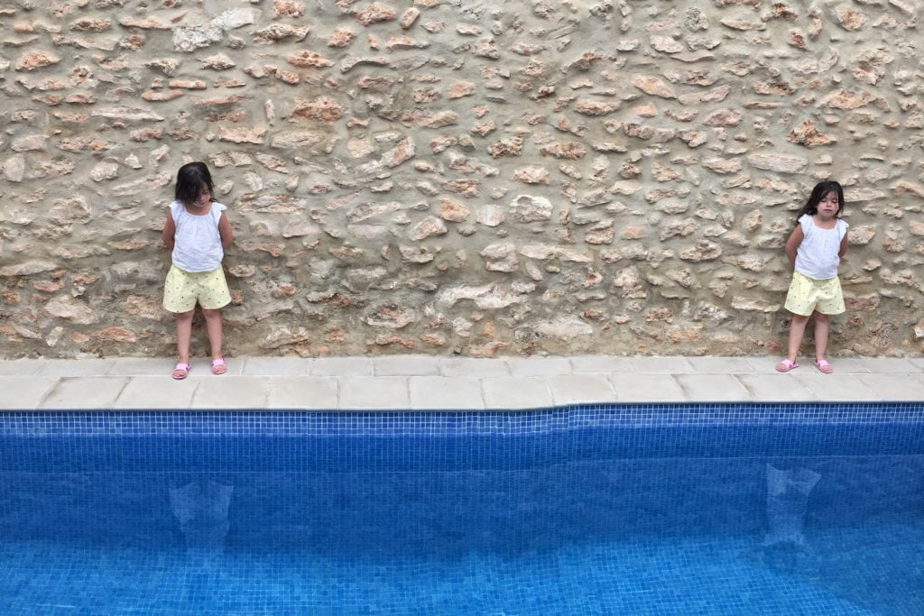 Niña clonada en piscina con fachada de piedra al fondo 