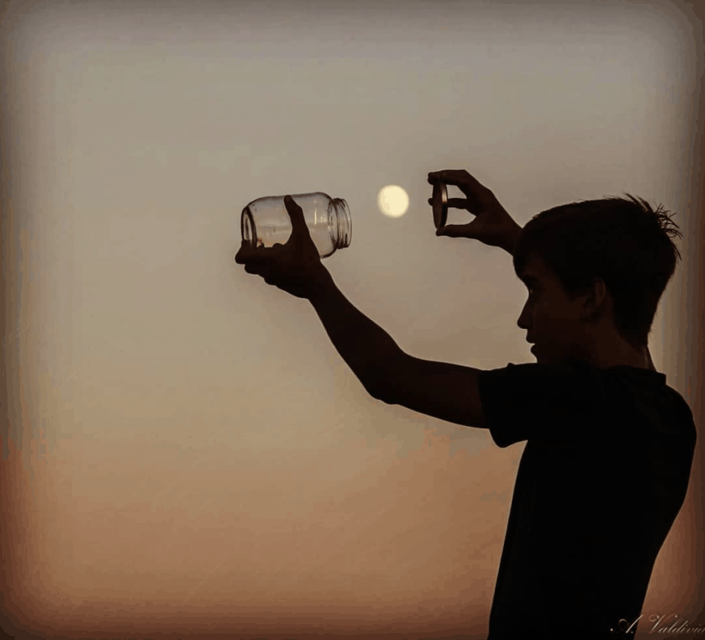 Silueta de niño cazando la luna con un bote de cristal