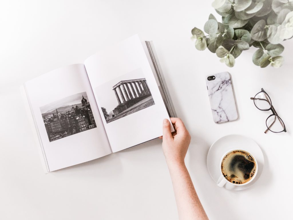 Libro de fotografía abierto, con mano pasando hojas y un café al lado