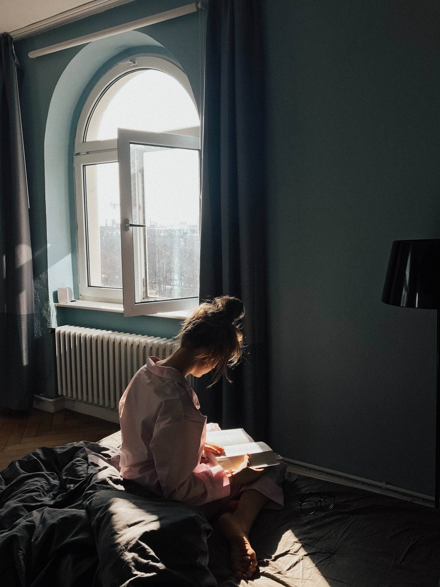 Lectora sentada en la cama bañada por la luz de una ventana