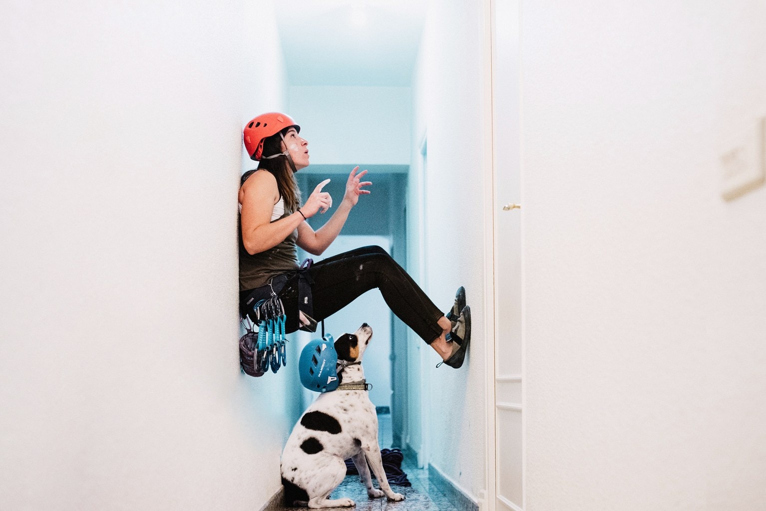 Autorretrato de chica escalando por pared de casa frente a la atenta mirada de su perro