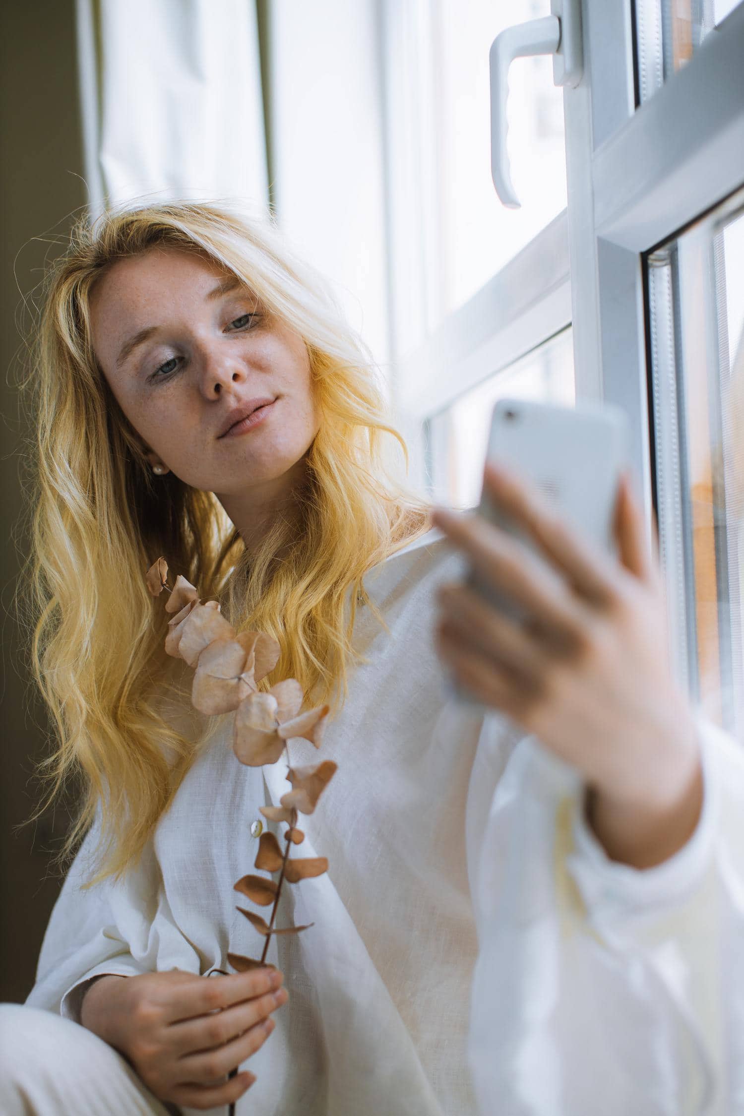 Chica haciéndose selfie con el móvil cerca de la ventana