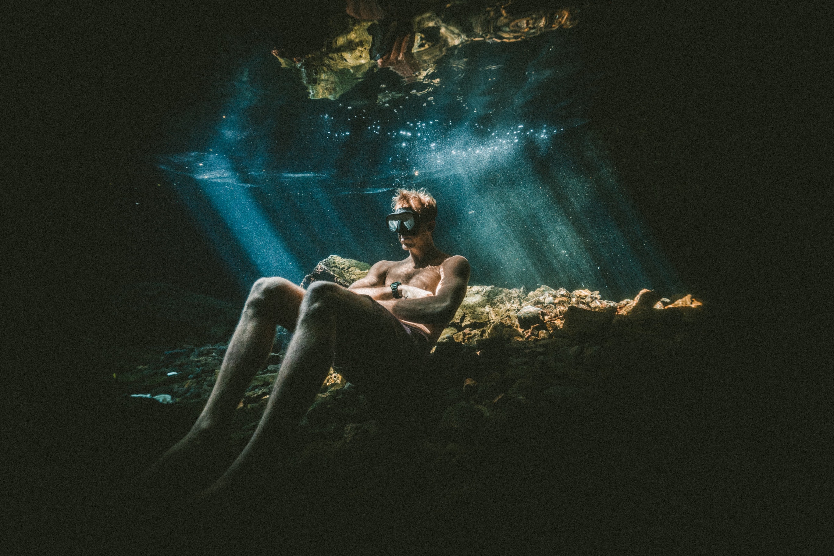 Man with diving goggles sitting on the rock under water