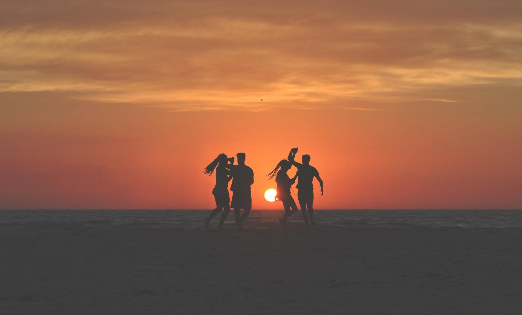 Siluetas bailando en la playa al atardecer para el fotoreto115 de vacaciones