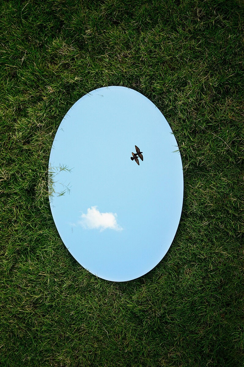 fotografía artística con espejo sobre la grama y reflejo del cielo