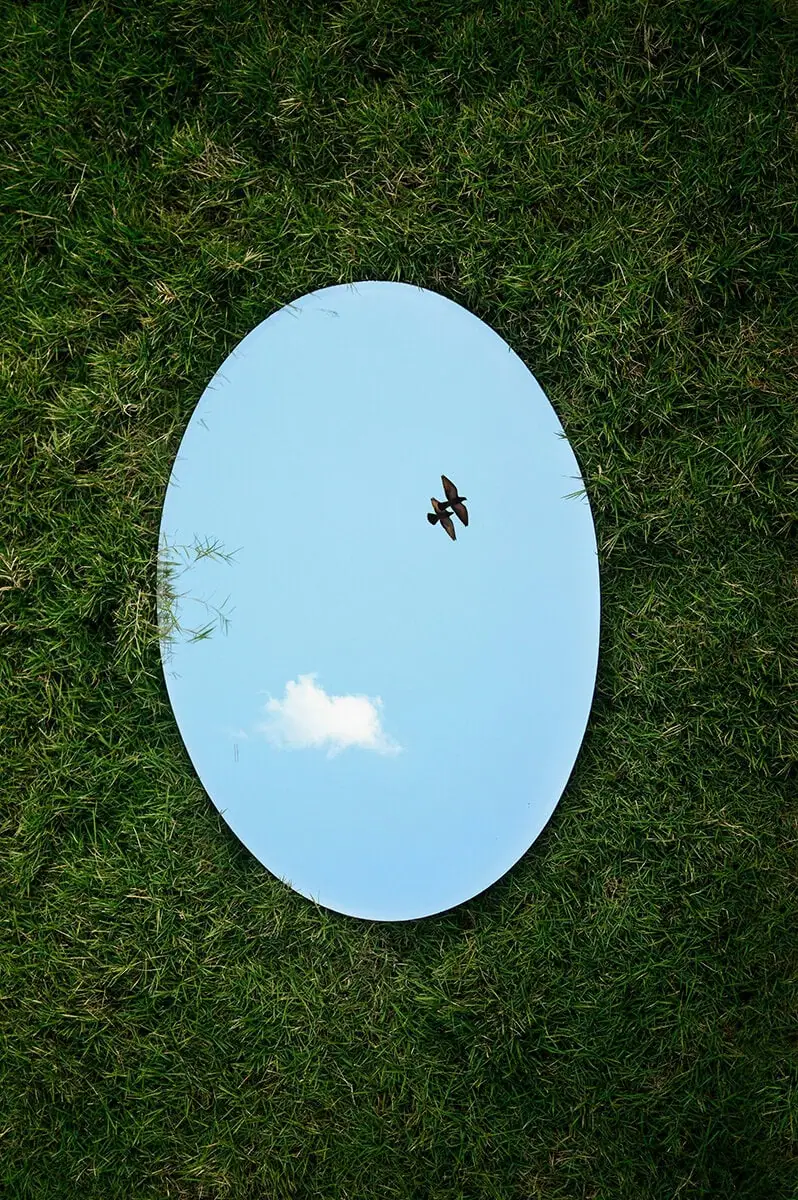 fotografía artística con espejo sobre la grama y reflejo del cielo