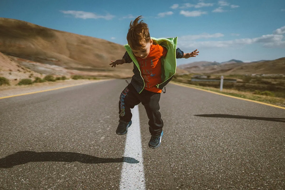 Niño saltando sobre una carretera capturado con uso back button focus