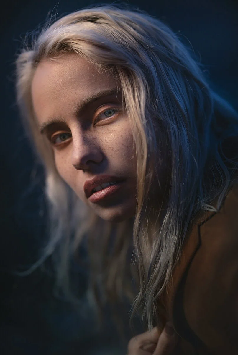 Retrato artístico con luz tenue de mujer rubia, capturado con un objetivo luminoso ideal para fotografía de retrato en condiciones de poca luz.