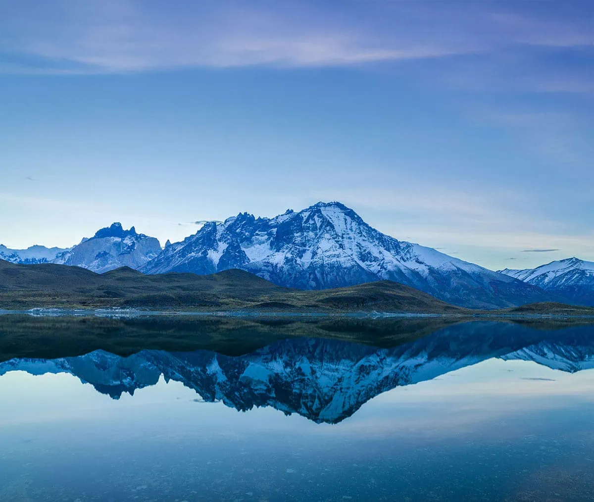 Fotografía de paisaje con montaña nevada reflejada en un lago tranquilo al atardecer