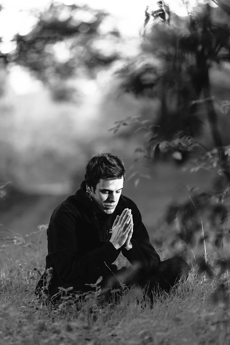 Retrato emocional en blanco y negro de hombre en oración, capturado con un teleobjetivo de 135mm para fotografía de retrato.